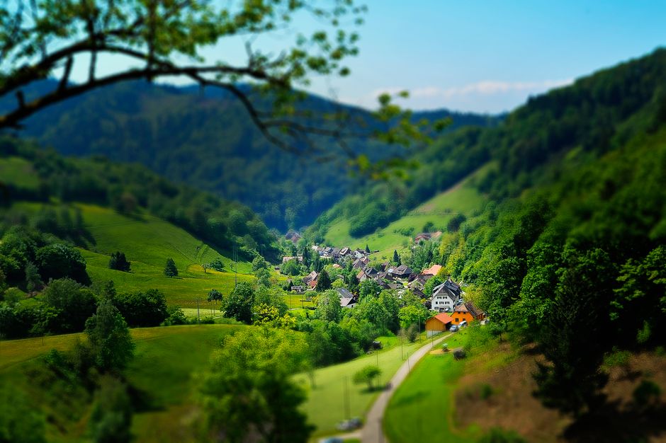Charming countryside village nestled in a lush, green valley under a bright blue sky.