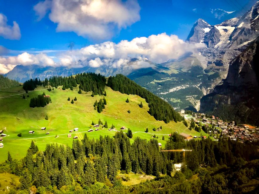 Picturesque alpine village surrounded by lush greenery and scenic mountains under a vibrant blue sky.